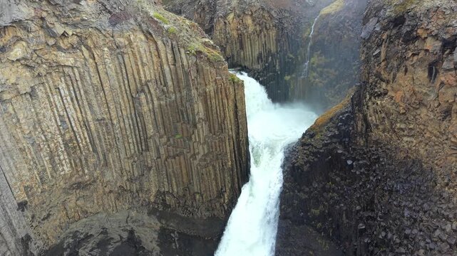 Stunning aerial perspective of Litlanesfoss waterfall. Powerful water carving its way through a deep canyon framed by unique basalt columns
