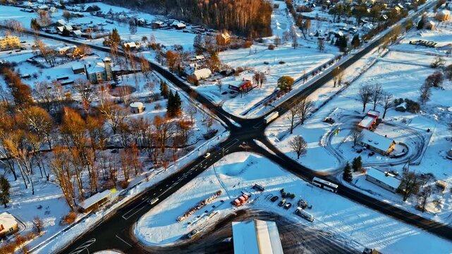 Aerial view of a snowy intersection with surrounding buildings, trees, and vehicles on the road in Jelgava, Latvia.