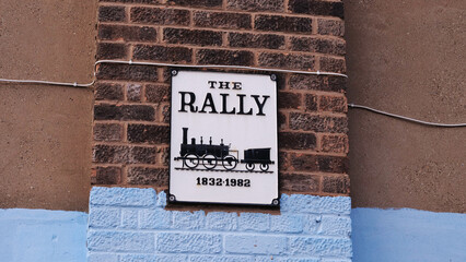 The Rally pub sign featuring locomotive silhouette and 1832-1982 dates mounted on brick wall © Adrenaloby
