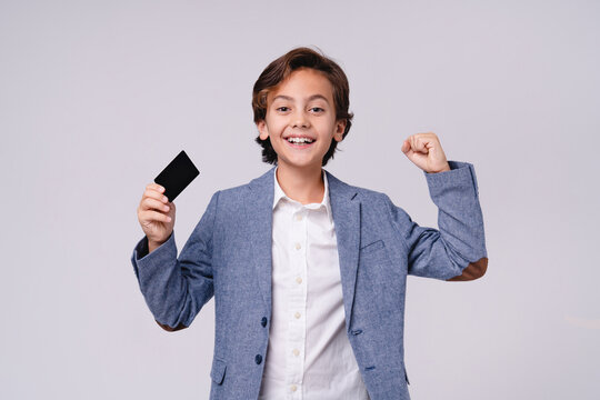 Happy Caucasian boy celebrating like a winner with credit card isolated on grey background, childhood, finance, payment, shopping, success and future businessman concept