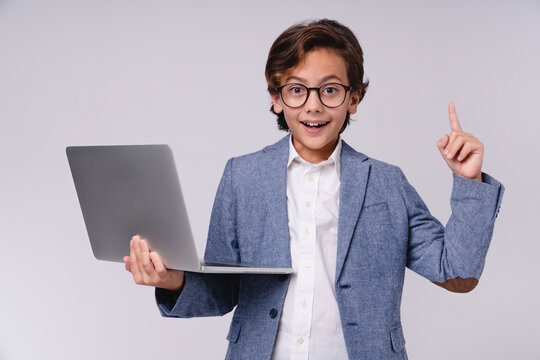 Young small boy in formal outfit having an idea while holding a laptop isolated on grey background, childhood, technology, education, future businessman, creativity, career and professional concept