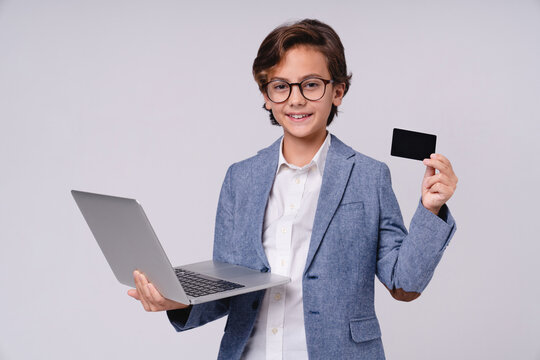Confident little boy in formal attire holding credit card and laptop isolated on grey background, childhood, technology, finance, online shopping, future businessman and success concept