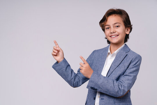 Successful young boy pointing at copy space in formal clothes isolated on grey background, childhood, future businessman, leadership, career, success, presentation and professional concept