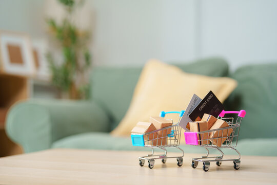 Shopping carts with package boxes and credit cards on table in home interior with copy space, online shopping, e-commerce, retail purchase, payment, consumer spending, order, shipping and delivery