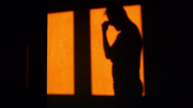 Silhouette of a depressed man on orange background. Pacing anxiously around the room and rubbing temples in a headache