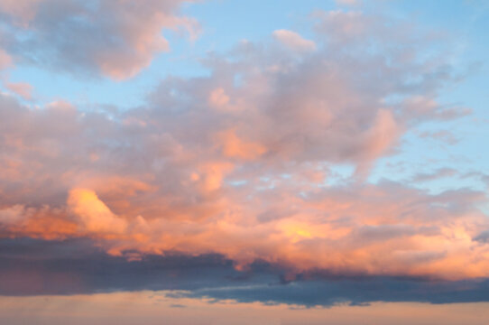 Blurry sky background. Fluffy clouds illuminated in bright pink and orange tones. Evening sunset light shining against a clear blue sky in the distance