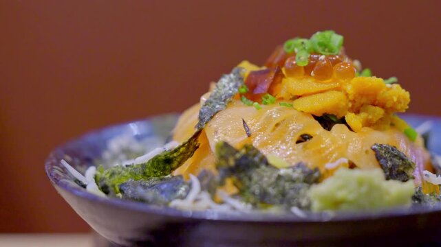 Close-up of a premium donburi bowl topped with assorted sashimi, creamy uni, and vibrant salmon roe over steamed sushi rice, beautifully arranged for an elegant Japanese meal.