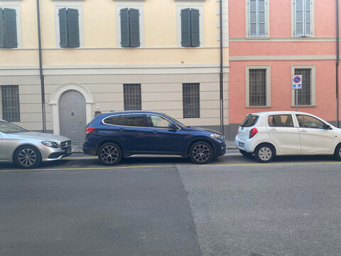 Modern cars including Mercedes Benz, BMW, and Suzuki parked along a colorful street, showcasing European urban daily life