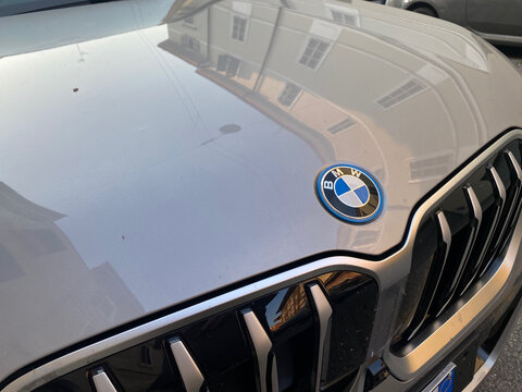 BMW badge on a modern car hood with reflection of buildings, emphasizing luxury and automotive branding