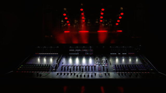 Professional audio mixing console with illuminated faders and buttons in dark concert venue