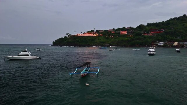 Aerial view of Amed Beach with traditional jukung boats and yachts anchored in the bay at dusk in Bali, Indonesia.
