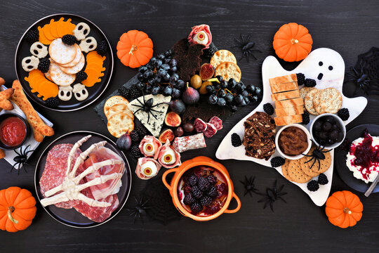 Halloween theme grazing table scene against a black wood background. Spooky charcuterie boards of meat and cheese appetizers. Top down.