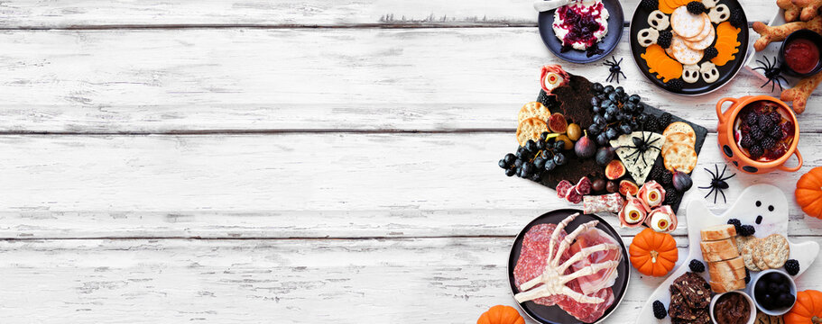 Halloween theme grazing side border against a white wood banner background. Spooky charcuterie boards of meat and cheese appetizers. Above view with copy space.