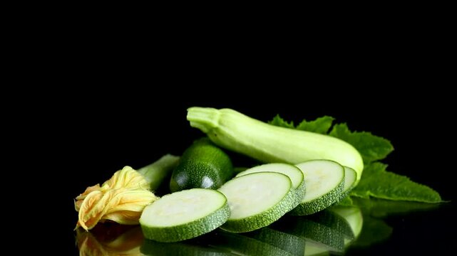 Garden grown zucchini squash with fresh leaves on black reflective background