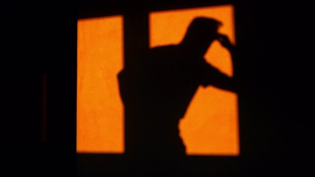 Silhouette of a depressed man on orange background. Pacing anxiously around the room and rubbing temples in pain from a migraine or a headache