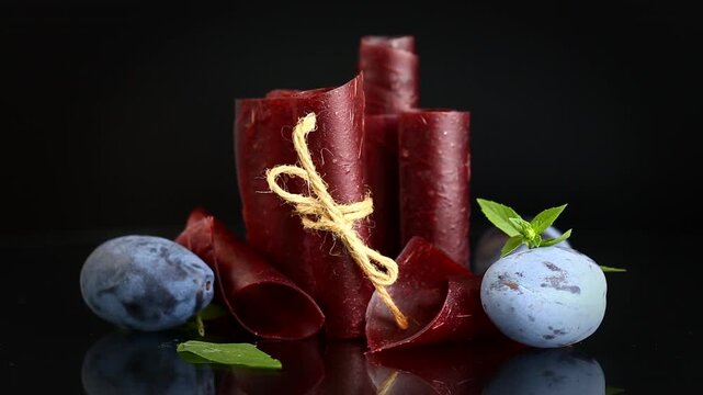 Sweet plum fruit leather rolls reflected on elegant black surface