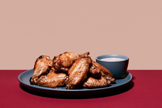 Spicy grilled chicken wings with charred skin on a dark platter beside dipping sauce, rustic and savory for restaurant menus and game-day advertising