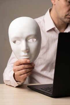 Person Holding Blank Mask Beside Laptop in Studio