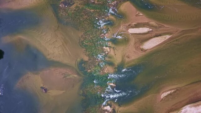 Loire River at exceptionally low water reveals broad exposed sandbars, shallow channels, aquatic vegetation and textured sediment patterns along the riverbed, France, drone top down flyover