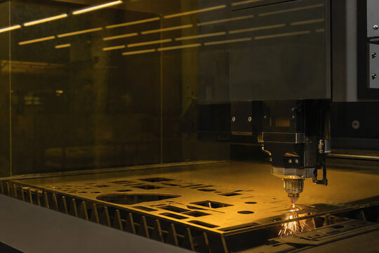 Industrial laser cutter machine processing metal sheet in workshop. Automated CNC equipment performing precision steel cutting. High technology manufacturing, metalworking production process.