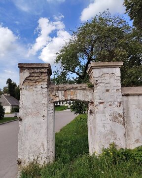 Ancient ruined brick gate and stone wall with peeling white stucco against blue sky with clouds