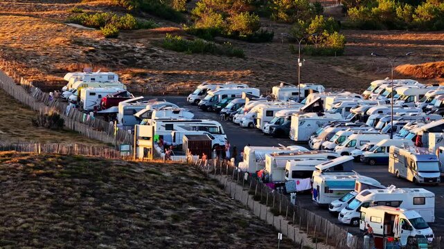 Camper vans fill a coastal parking area beside dunes at Plage des Oceanides, France, aerial tracking right