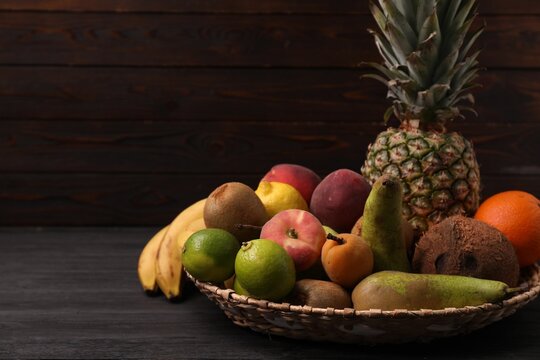Different fresh fruits in wicker basket on black wooden table, closeup. Space for text