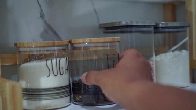 Person organizing glass jar contain tea on kitchen shelf, empty container, food storage and routine concept.