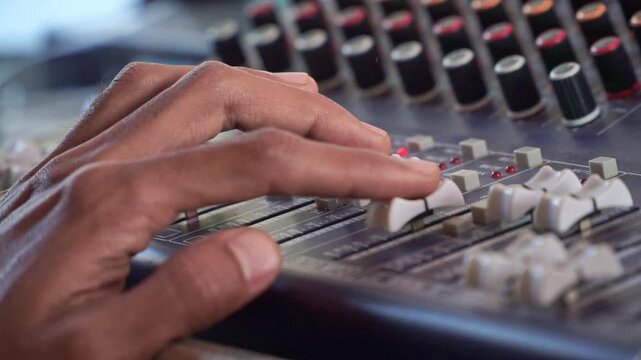 sound technician adjusting mixer knobs, audio console with LED meters, music production concept.
