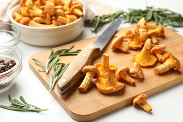 Wooden board with chanterelle mushrooms, knife, rosemary and spices on white table, closeup © New Africa
