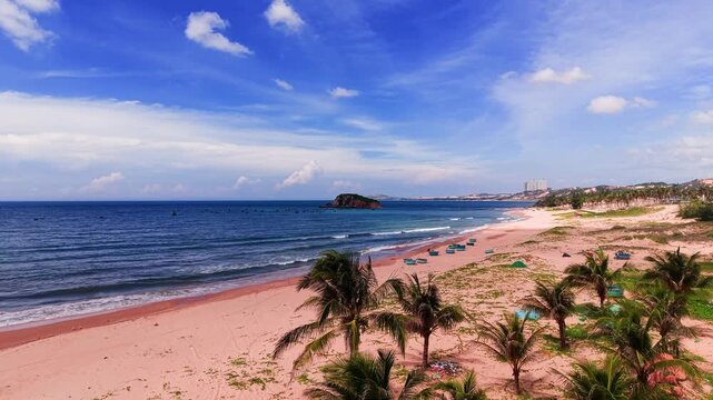 At Hoa Thang, Lam Dong, people enjoy the beach with calm waves and sandy shores. Sunlight shines brightly as they relax and take in the views of the ocean and distant land.