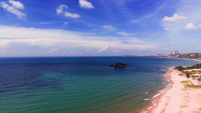 A view of the coast in Hoa Thang, Lam Dong. Waves crash on the shore while the sun shines. People walk along the beach, enjoying this natural setting.