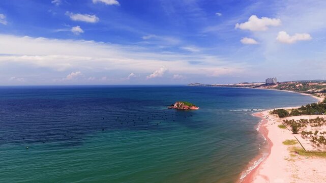 Visitors walk along the beach at Hoa Thang, Lam Dong. The sun shines brightly on the water, creating waves along the shore. People enjoy the sound of the ocean and relax under the blue sky.