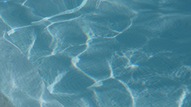 Sunlight caustics rippling across clear blue swimming pool water surface