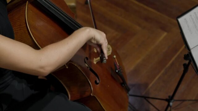 Close up of a musician drawing the bow across cello strings next to a music stand