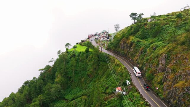 Drone flies forward as cars travel Halsema Highroad beside green mountain farms