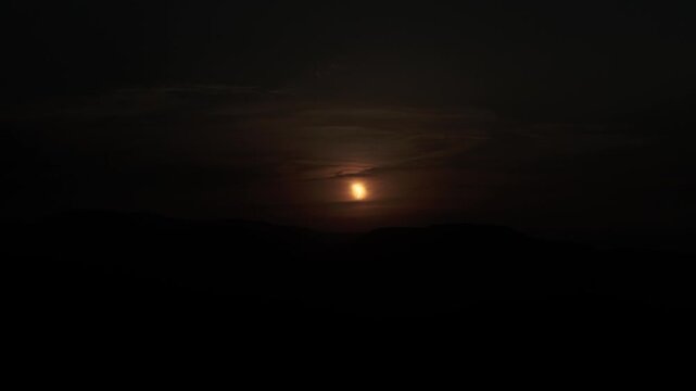 Partial solar eclipse over dark hills with dramatic clouds at dusk or dawn