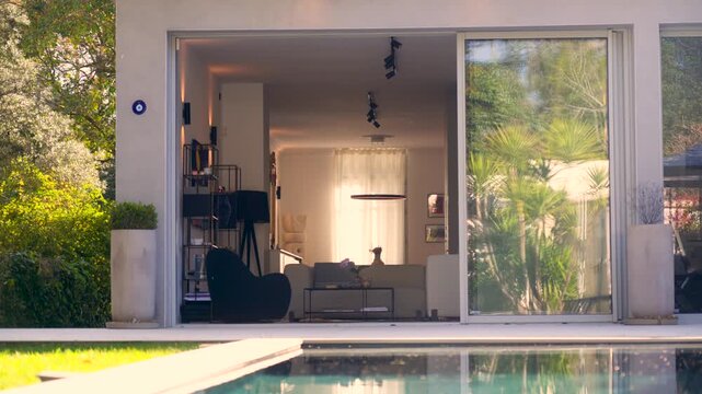 Modern house with open living room and poolside view, surrounded by greenery