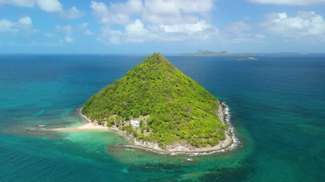 Aerial orbit circles pyramid shaped Sugar Loaf Island in Grenadines, showing forested peak, white sand beach, turquoise coral reef and clear Caribbean water