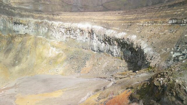 Aerial orbit circles steep layered crater walls streaked with sulfur white and rust orange minerals inside Soufri&egrave;re Volcano in Saint Vincent