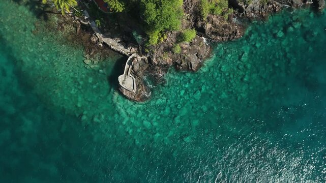 Top down aerial flies along Young Island's rocky shoreline over transparent turquoise water and coral reef, Saint Vincent