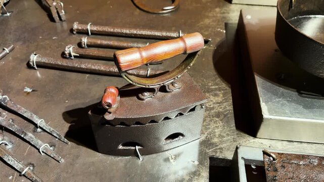 Antique blacksmithing tools and metal implements arranged on worn workshop bench, static still-life