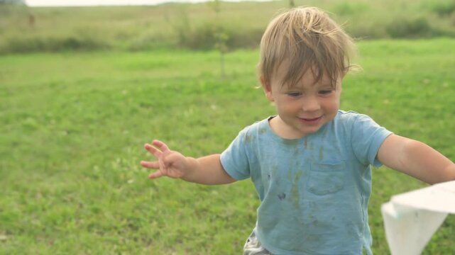 Toddler boy holding up a hand-decorated paper airplane and smiling in garden