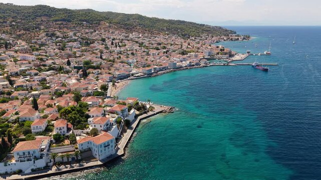 Spetses Town's terracotta rooftops and elegant neoclassical mansions cascade toward a brilliant turquoise coastline. The Dapia harbor and pine-covered hills stretch across this cosmopolitan Greek isla