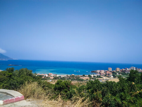 Panoramic high angle view capturing a scenic coastal town nestled along the vibrant turquoise Mediterranean sea under a clear bright sunny summer sky in northern Algeria.