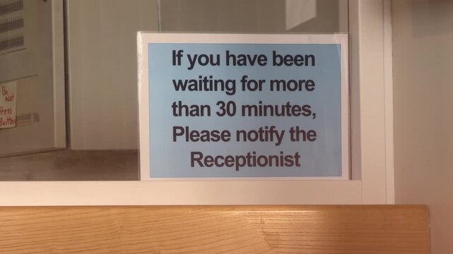 Close-up view, reception notice in Kilmarnock, Scotland, advising visitors who have waited more than 30 minutes to notify the receptionist