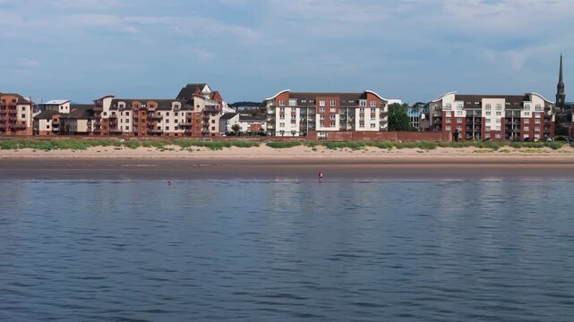 Aerial panning view, along sandy Beach and residential apartments in Ayr, South Ayrshire, Scotland, on a bright summer day