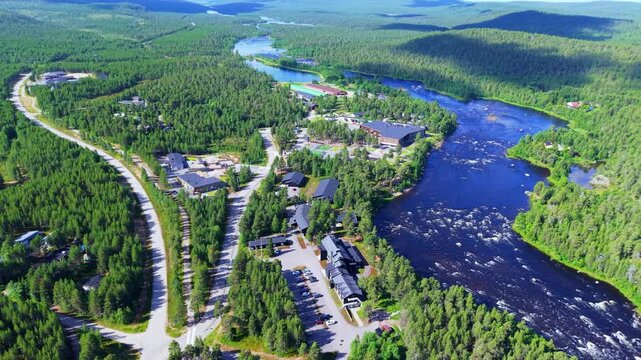 Aerial view over the Juutua River in Inari, Finnish Lapland, showing rapids, riverside buildings, roads and dense boreal forest near the river&rsquo;s mouth toward Lake Inari in northern Finland