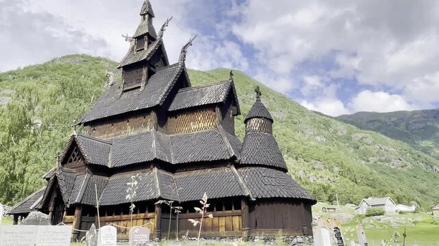 View of the medieval Borgund Stave Church in L&aelig;rdal, Norway, featuring distinctive layered wooden roofs, traditional stave architecture and dramatic green mountain scenery