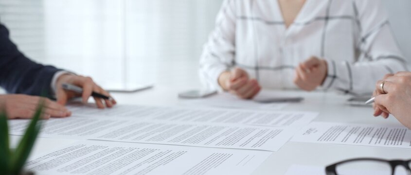 Business people discussing contract documents on a white desk, analyzing clauses and terms during an office meeting, collaborating on important paperwork for agreement